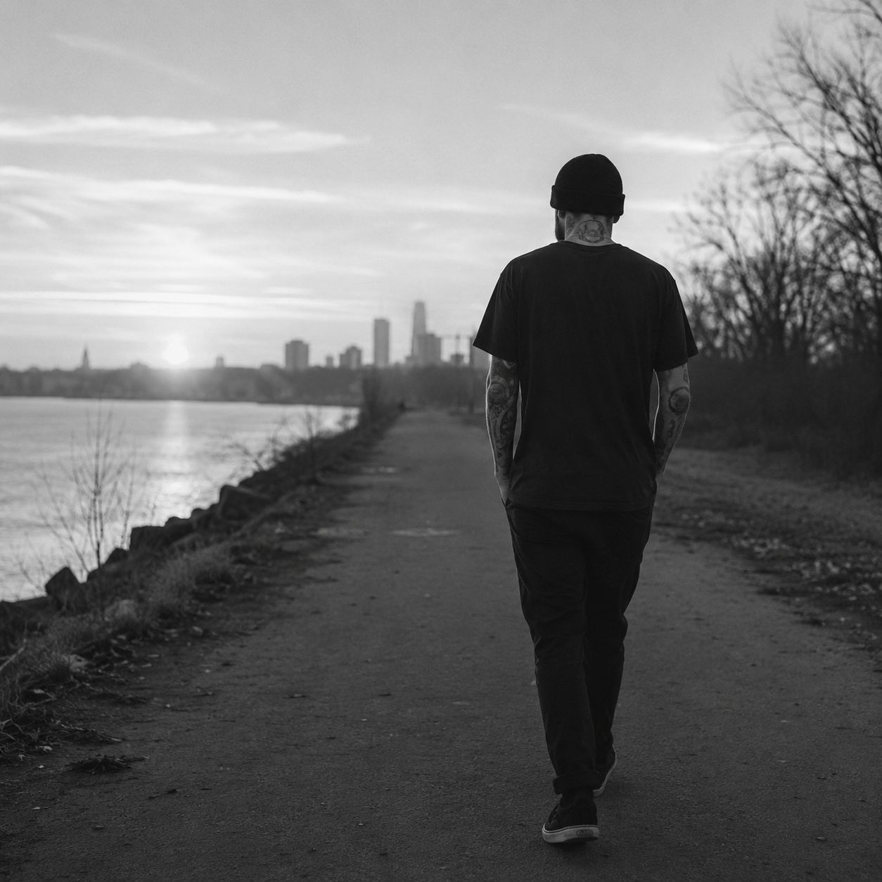A man walking along a lakeshore path at first light, the city skyline behind him